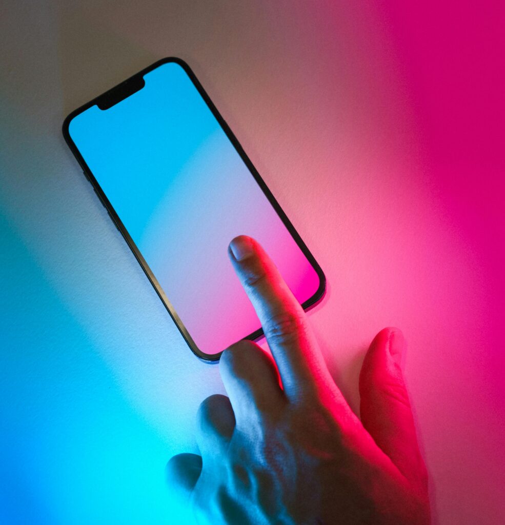 pexels-photo-27788817-27788817 A hand interacts with a glowing smartphone screen in a neon-lit setting, featuring vibrant gradient colors.
