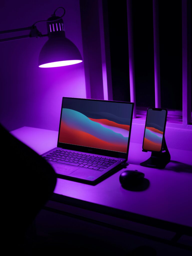 pexels-photo-5948347-5948347 A sleek desk setup with a laptop and smartphone under purple lighting. High-tech and stylish.